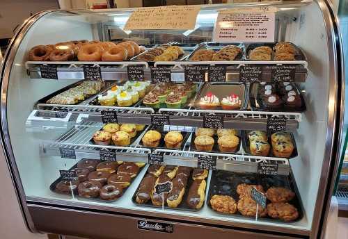 A display case filled with various baked goods, including donuts, pastries, and muffins, with price tags visible.