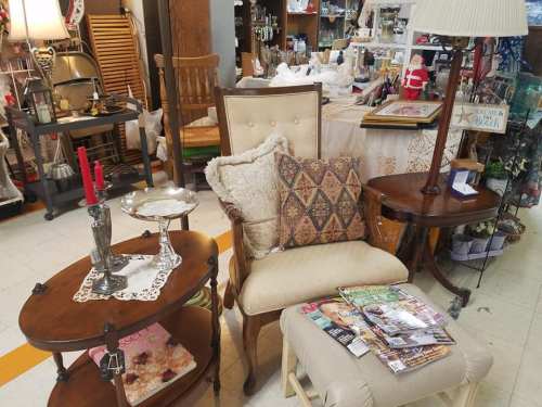 A cozy display of vintage furniture, including a chair, side tables, and decorative items in a shop setting.