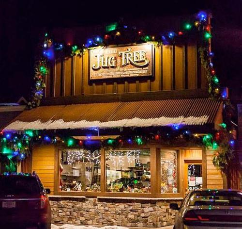 A warmly lit store, "Jug Tree," decorated with colorful holiday lights and garlands, set against a snowy night backdrop.