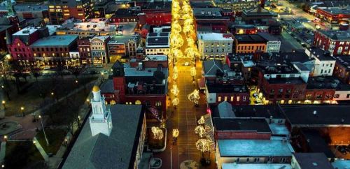 Aerial view of a city street illuminated with festive lights, showcasing buildings and a vibrant holiday atmosphere.