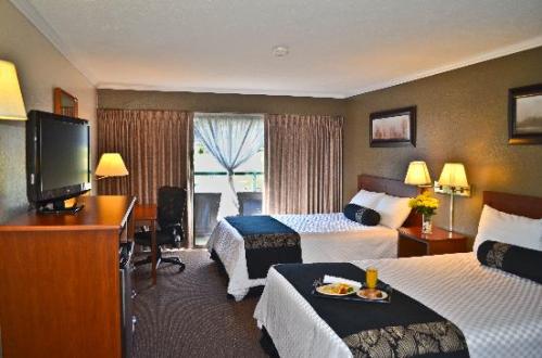 A cozy hotel room with two beds, a TV, and a balcony door, featuring a breakfast tray on the table.