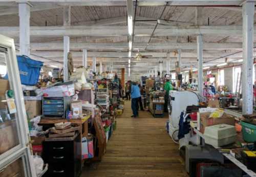 A spacious antique shop filled with various items, including furniture, boxes, and collectibles, with a person browsing.