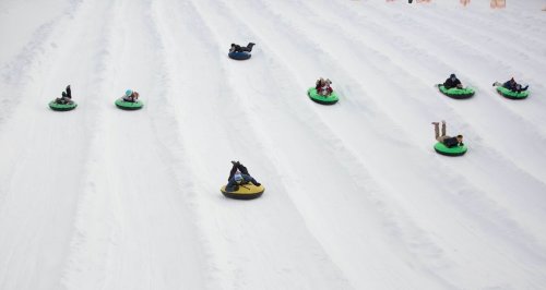A snowy hill with several people tubing down on colorful inflatable tubes.