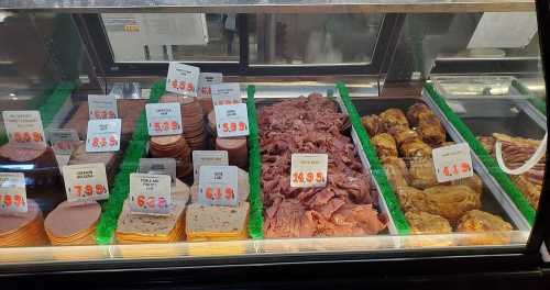 Deli display featuring various meats and cheeses with price tags, arranged neatly in a refrigerated case.