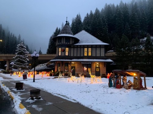 A snowy scene featuring a charming building with a tower, surrounded by festive lights and a nativity display.