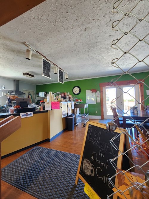 Cozy café interior with green walls, a counter, chalkboard menus, and a welcome sign at the entrance.