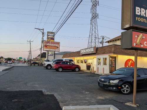 A street view of a restaurant called "Dog House" with parked cars and power lines at dusk.