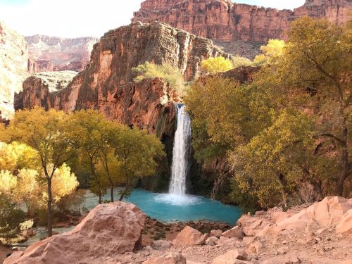 A serene waterfall cascades into a turquoise pool, surrounded by vibrant autumn trees and rocky cliffs.