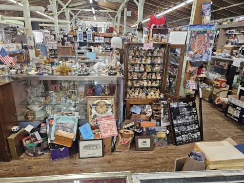 A cluttered antique shop filled with various collectibles, glass displays, and vintage items on wooden floors.