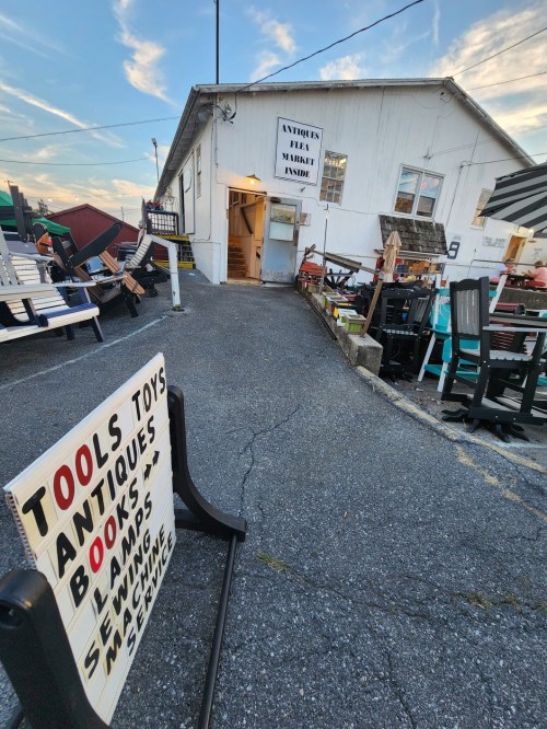 A sign advertising tools, toys, antiques, and books outside an antique market with various items displayed.