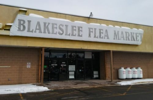 Exterior of Blakeslee Flea Market with a large sign, entrance doors, and snow on the ground.
