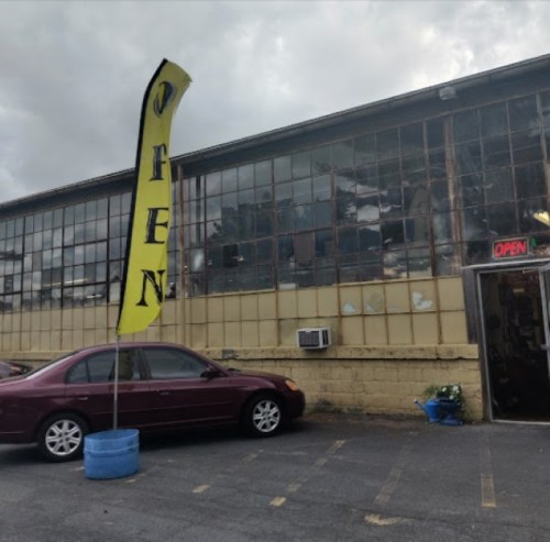 A building with large windows and an "OPEN" sign, featuring a car parked outside and a tall yellow flag.