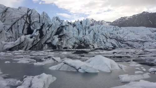 A stunning glacier with towering ice formations and a calm water surface, set against a mountainous backdrop.