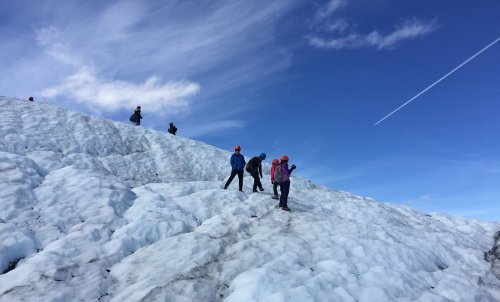 A group of climbers wearing helmets traverses a snowy glacier under a blue sky with wispy clouds.