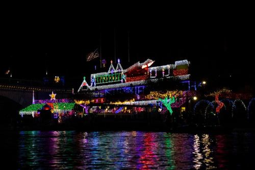 A brightly lit building adorned with colorful holiday lights, reflecting on the water at night.