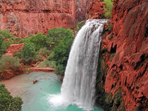 A stunning waterfall cascades into a turquoise pool, surrounded by red rock cliffs and lush greenery.