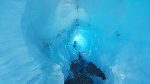 A stunning ice cave with vibrant blue walls and a bright light at the end, creating a serene, otherworldly atmosphere.