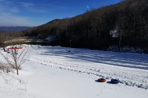 A snowy landscape with tire tubes on the ground, surrounded by trees and a hill under a clear blue sky.