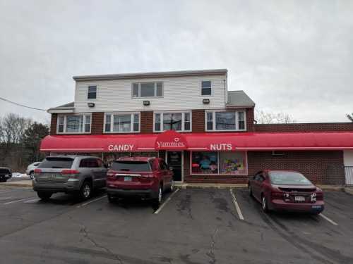 A storefront with a red awning labeled "Yummies" selling candy and nuts, featuring parked cars in front.