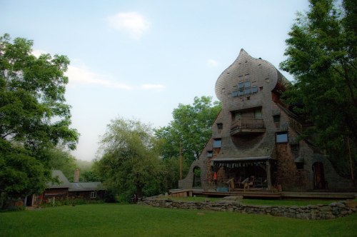 A unique, whimsical house with a curved roof and large windows, surrounded by lush greenery and a clear sky.
