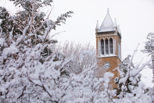 A snow-covered clock tower peeks through frosted trees in a winter landscape.