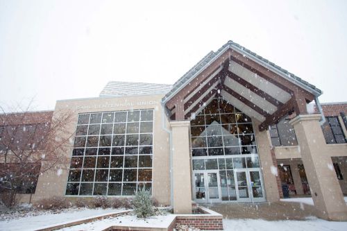 A snowy scene of the Paul Centennial Union building with large windows and a distinctive entrance.