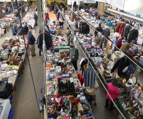 A bustling indoor market filled with tables of various items, including clothes, toys, and household goods.