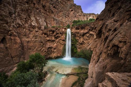 A stunning waterfall cascades into a turquoise pool, surrounded by rocky cliffs and lush greenery.