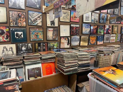 A cluttered record store with stacks of vinyl records and walls adorned with album covers.