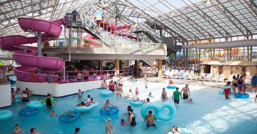 Indoor water park scene with colorful slides, pools, and people enjoying the water on inflatable tubes.