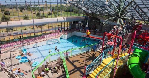 Indoor water park featuring a pool, water slides, and lounging areas, with people enjoying the attractions.