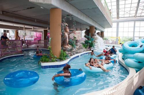 Indoor water park scene with people floating on tubes, a waterfall feature, and tropical decor.