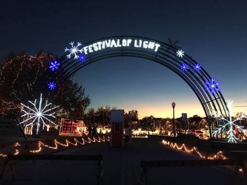 A festive archway reading "FESTIVAL OF LIGHT" adorned with lights and snowflake decorations at dusk.