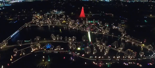 Aerial view of a festive park illuminated with colorful holiday lights, featuring a large red Christmas tree.