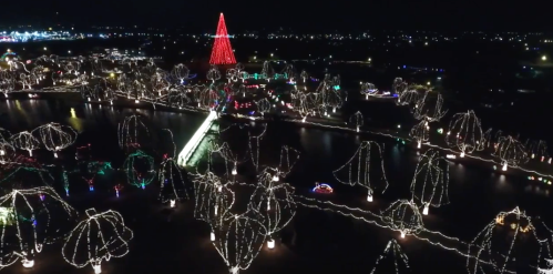 Aerial view of a festive park illuminated with colorful holiday lights, featuring a large red Christmas tree.