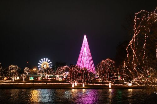 A festive scene featuring a large pink Christmas tree and colorful lights around a lake, with a ferris wheel in the background.