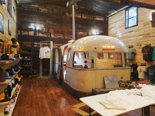 A vintage Airstream trailer inside a rustic wooden store, surrounded by clothing displays and merchandise.