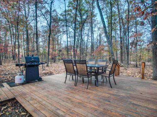 A wooden deck with a dining table and chairs, surrounded by trees in a forested area during autumn.
