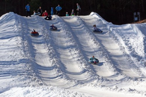 A snowy hill with people sledding down on tubes, enjoying a winter day outdoors.