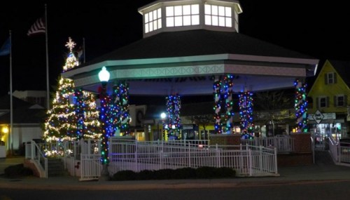 A festive gazebo decorated with colorful lights and a Christmas tree at night, creating a cheerful holiday atmosphere.