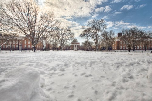 A snowy landscape with bare trees and historic buildings under a cloudy sky.