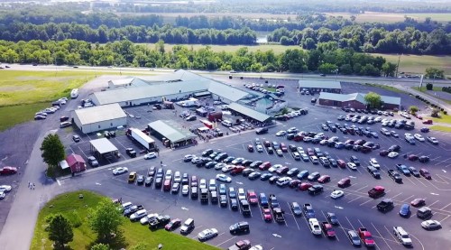 Aerial view of a large parking lot filled with cars, adjacent to a building and surrounded by greenery.