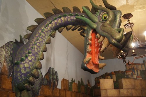 A colorful dragon sculpture with a long neck and open mouth, mounted on a wall in a whimsical setting.
