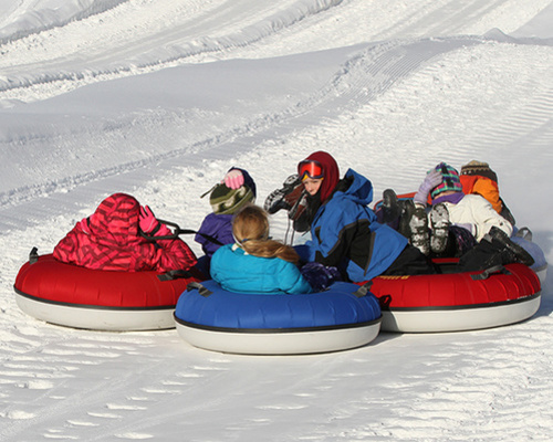 A group of children in colorful winter clothing tubing down a snowy hill, enjoying a fun day in the snow.