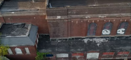 Aerial view of an old, abandoned brick building with broken windows and graffiti on the roof.