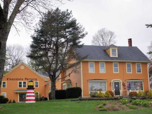 A charming orange house with a sign reading "Chocolate Factory" and a red and white striped lighthouse nearby.