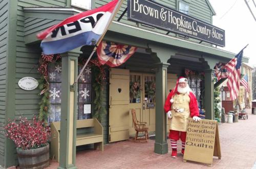 A festive country store with a Santa figure outside, decorated for the holidays, featuring an "OPEN" sign and American flags.