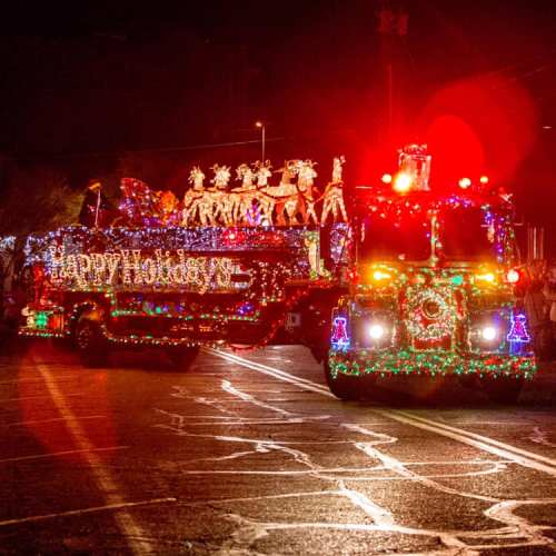 A festive parade float decorated with colorful lights and holiday decorations, moving down a street at night.