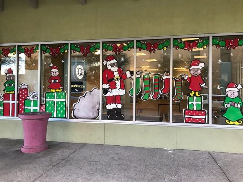Colorful holiday window display featuring Santa, gifts, stockings, and festive characters.