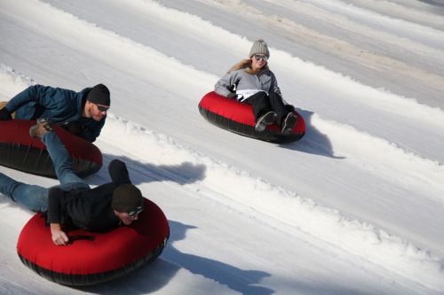 Three people are tubing down a snowy slope, each on red inflatable tubes, enjoying a winter day.